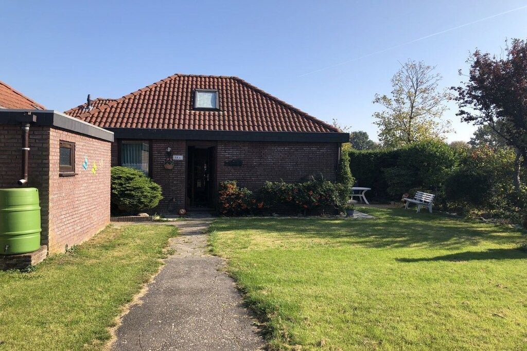 A single-story brick building with a tiled roof, a small window, and a door. There is a paved path leading to the entrance, and a grassy area with a bench and a table.