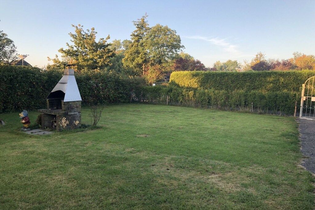A backyard with a stone barbecue grill, a hedge, and a grassy lawn.