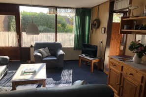 A living room with a sofa, armchair, coffee table, TV, and a wooden cabinet. - Holiday apartment in Herkingen with barbecue (Herkingen)