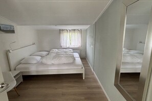 A bedroom with a single bed, a bedside table, a mirror, and a window with curtains. - Holiday apartment with 3 bedrooms (Ballum (watteninseln))