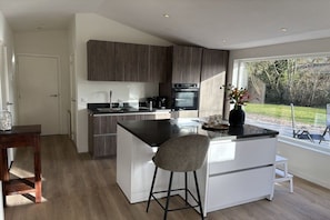 Een moderne keuken met een centraal eiland, donker houten kastjes en uitzicht op een tuin door een groot raam.