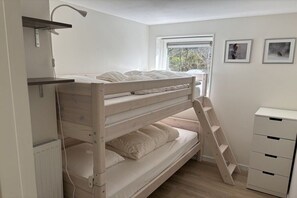 Een stapelbed met een ladder, een bureau met lades en een radiator.