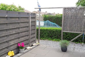 A fenced outdoor area with a potted plant, a small garden, and a blue flag on a pole. - Holiday apartment with 1 bedroom (Zoutelande)