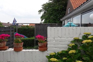 A residential area with a white brick wall, potted plants, and a blue flag. - Holiday apartment with 1 bedroom (Zoutelande)