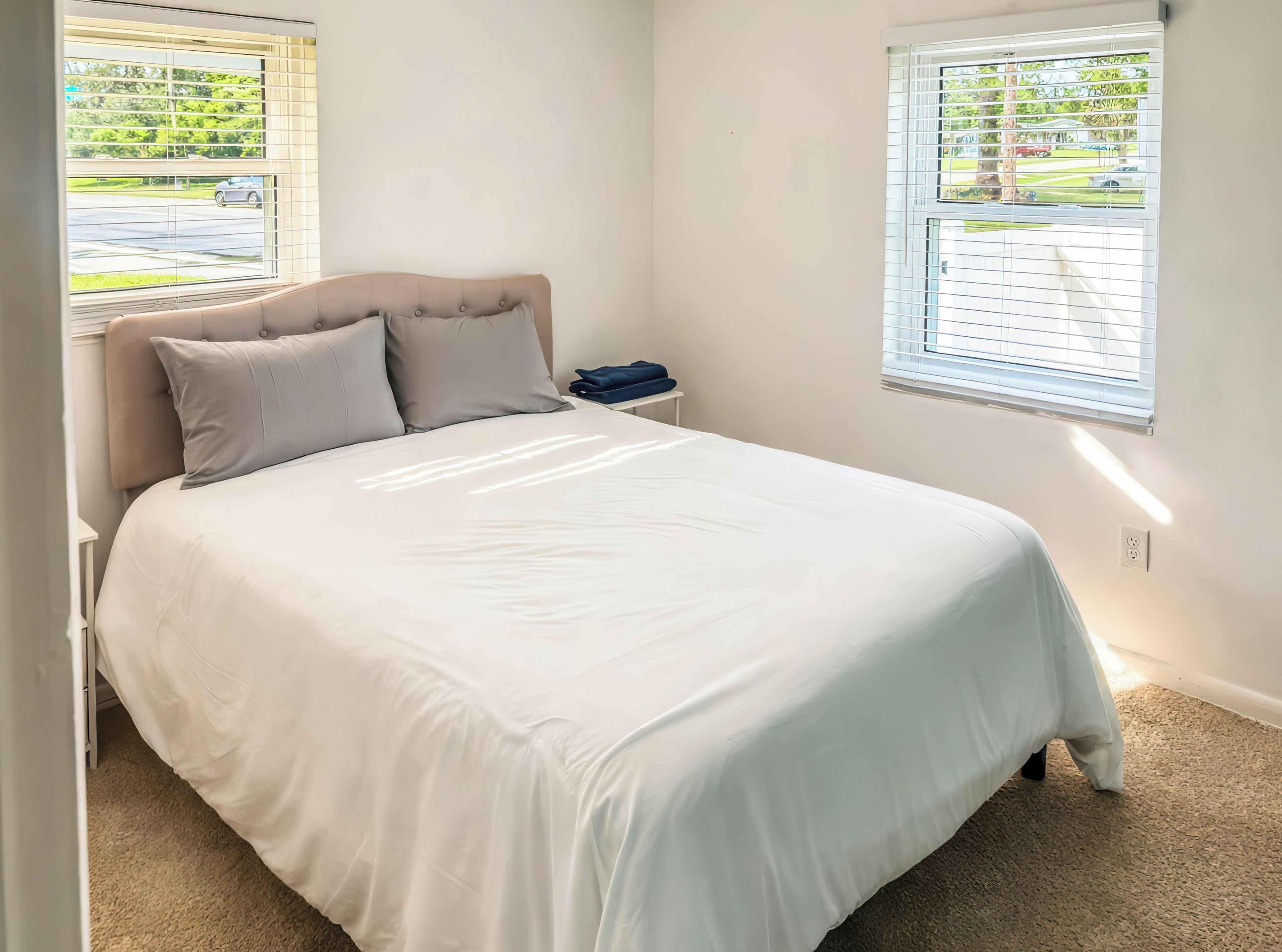 Un dormitorio con cama, dos ventanas y una mesita de noche.