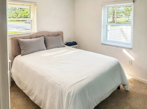 Un dormitorio con cama, dos ventanas y una mesita de noche.