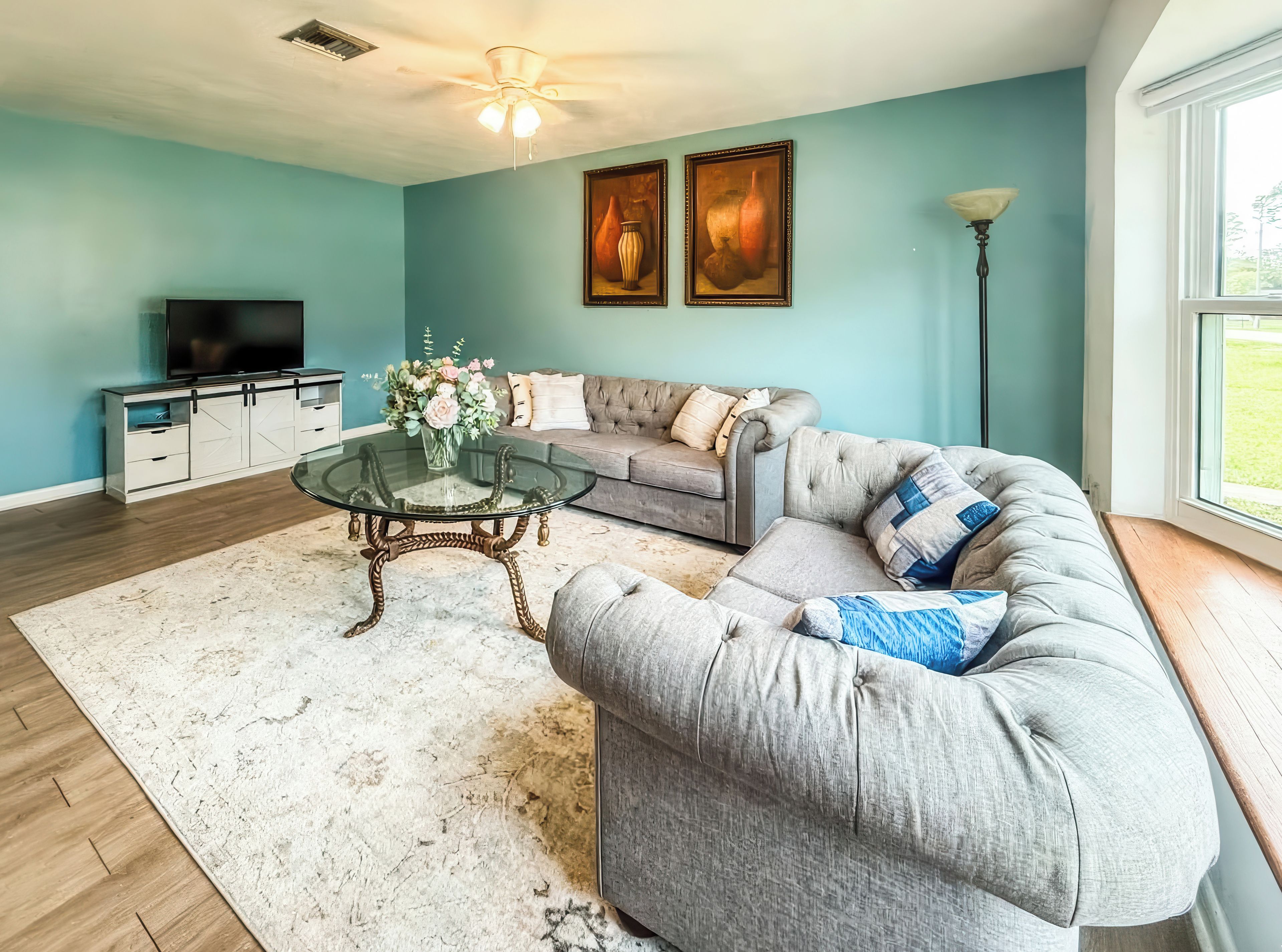 A living room with a sofa, a glass coffee table, a TV, and artwork on the wall.