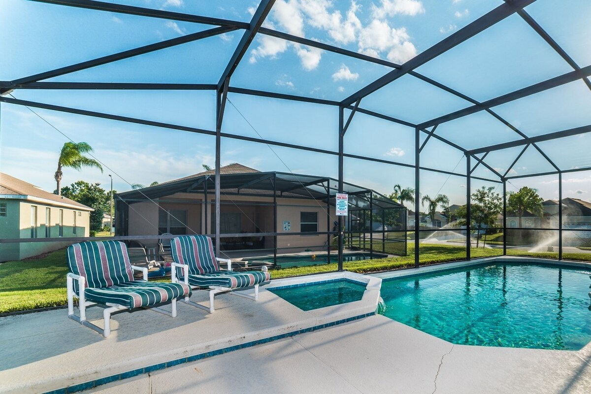 A pool area with a clear view of the sky, a pool, and a covered seating area with chairs.