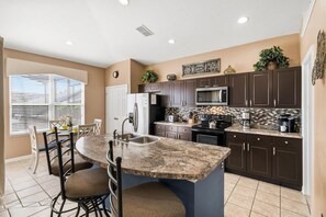 A modern kitchen with dark brown cabinets, a granite countertop, and a built-in microwave. - Fp8157 4 Bedroom Home (Kissimmee)