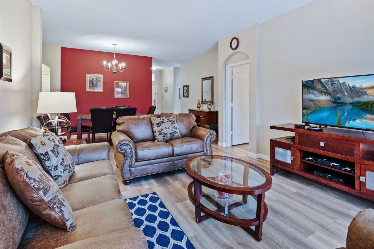 A living room with a leather sofa, a glass coffee table, and a wooden entertainment unit with a flat-screen TV.