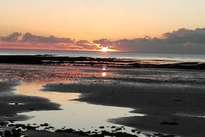 Ein Strand mit Sonnenuntergang, feuchtem Sand und ruhiger See.