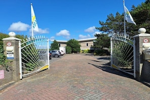 A gated entrance with a clear path leading to a building, a speed limit sign of 15, and flags on poles. - Apartment in Julianadorp with swimming pool (Julianadorp)