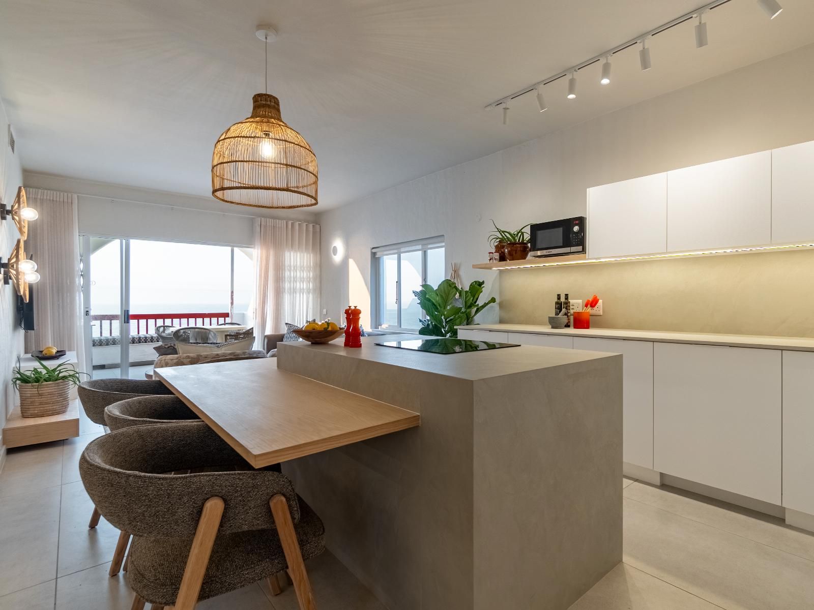 Una cocina moderna con una isla central, sillas de comedor y una lámpara colgante.