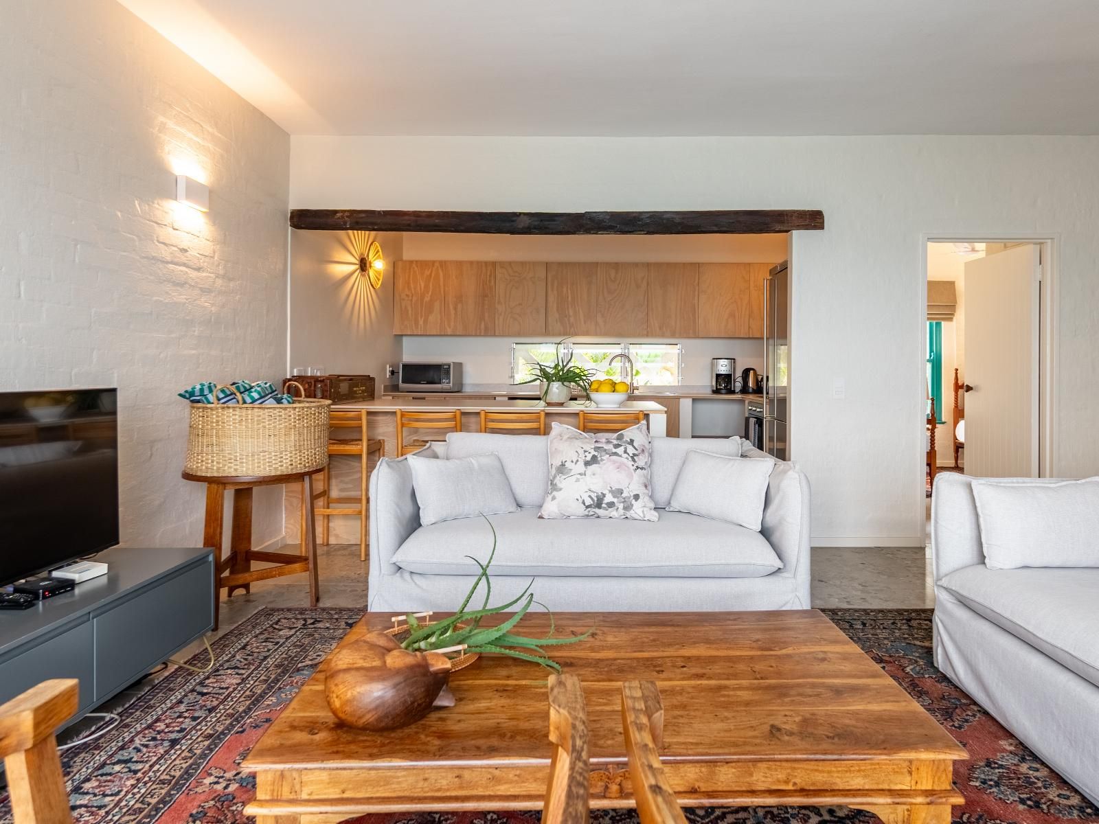 Una sala de estar moderna con un sofá, una mesa de centro con un cuenco decorativo, un televisor y una cocina al fondo.