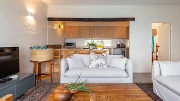 Una sala de estar moderna con un sofá, una mesa de centro con un cuenco decorativo, un televisor y una cocina al fondo.
