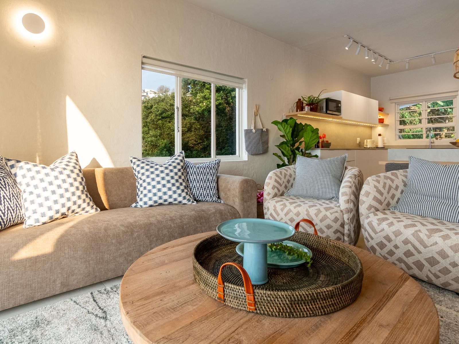 Una sala de estar moderna con un conjunto de sofás, una mesa redonda de centro con un adorno azul, y una cocina al fondo.