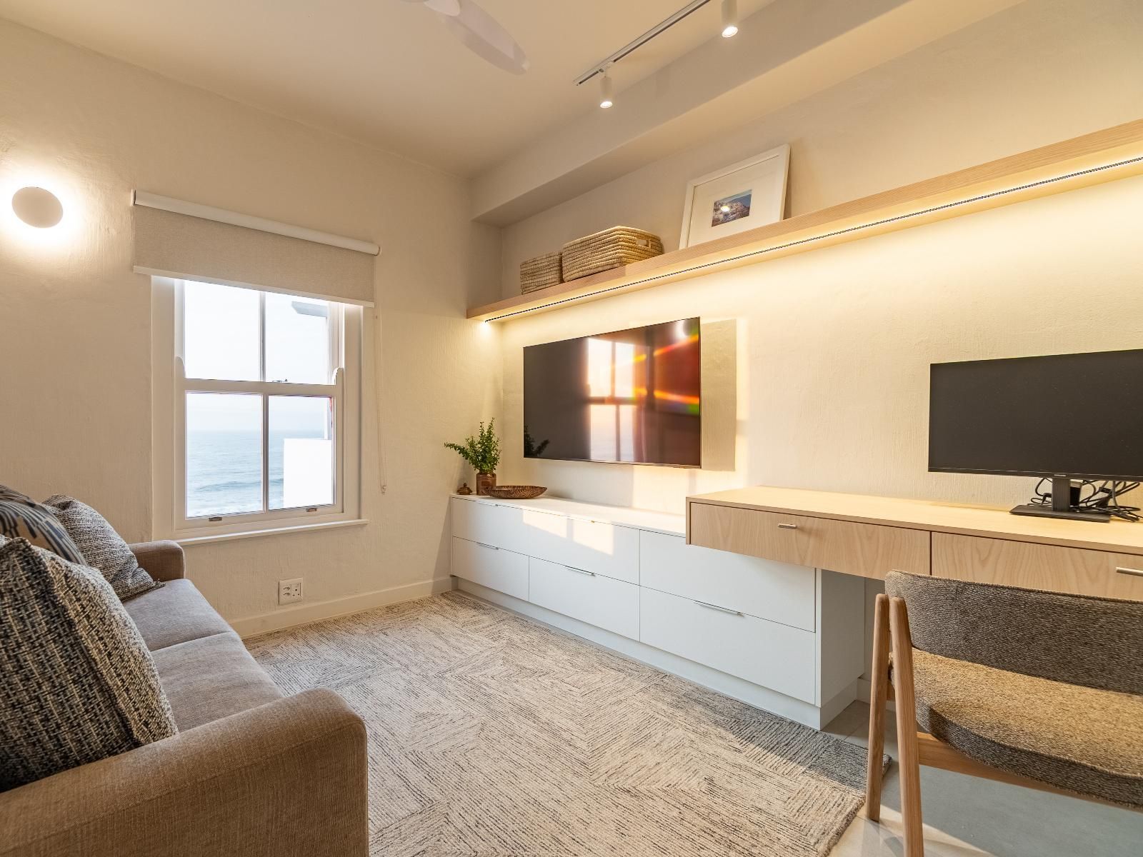 Una sala de estar moderna con un sofá, un escritorio, un televisor y una ventana con vistas al mar.
