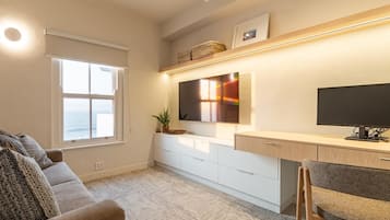 Una sala de estar moderna con un sofá, un escritorio, un televisor y una ventana con vistas al mar.