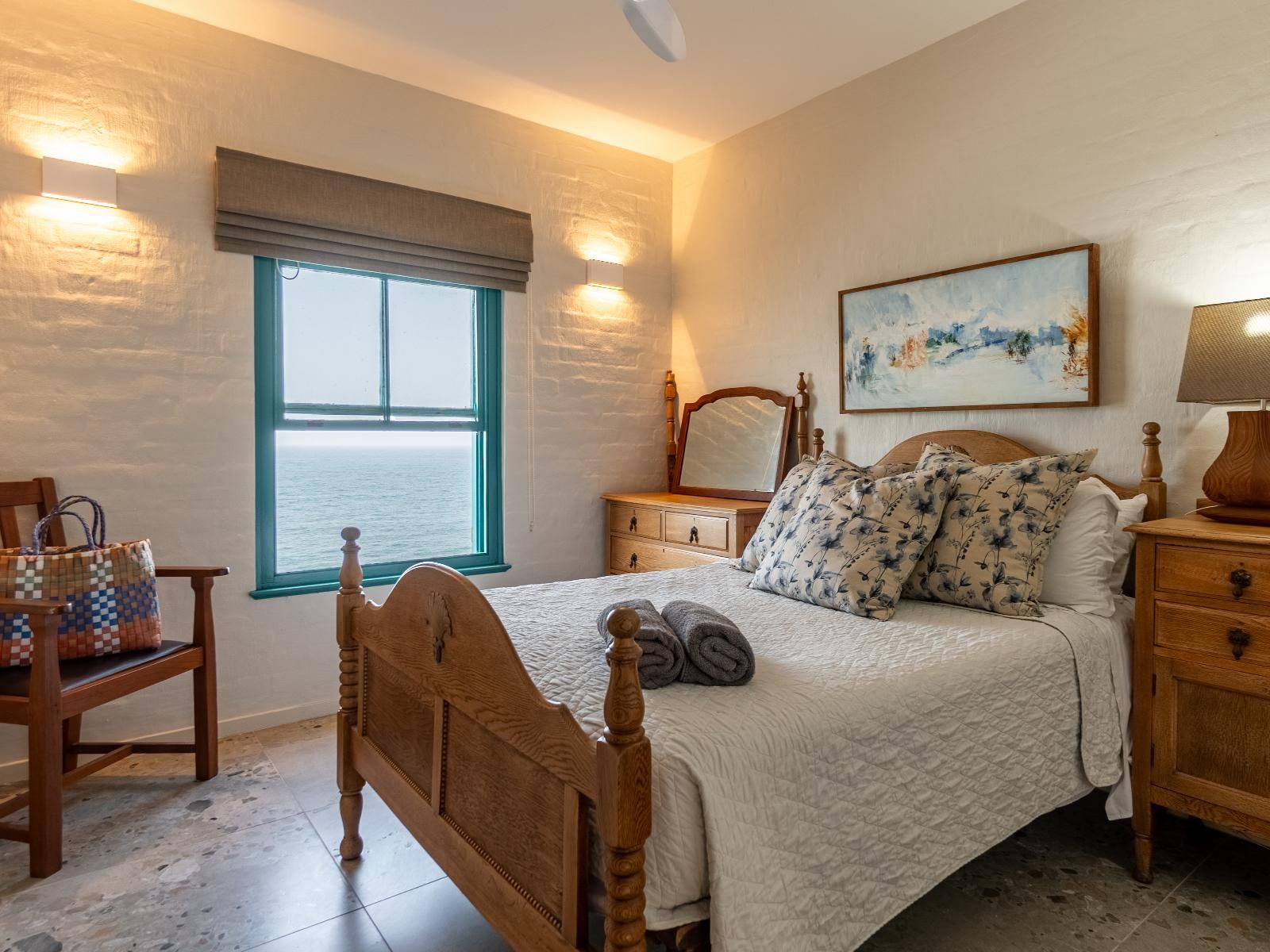 Un dormitorio con una cama grande, una mesita de noche, una silla, un ventanal con vistas y un cuadro en la pared.