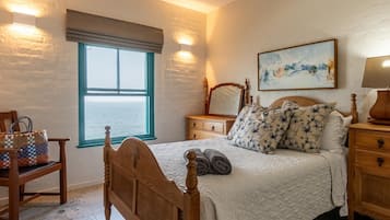 Un dormitorio con una cama grande, una mesita de noche, una silla, un ventanal con vistas y un cuadro en la pared.
