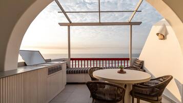 Un espacio al aire libre iluminado por el sol con una mesa redonda y sillas de mimbre, con vista a un cuerpo de agua.