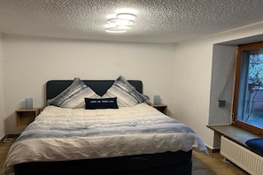 A bedroom with a bed, two bedside tables, a nightstand, a window with a view, and a ceiling light fixture. - UferZeit holiday home with terrace (Ediger-Eller)