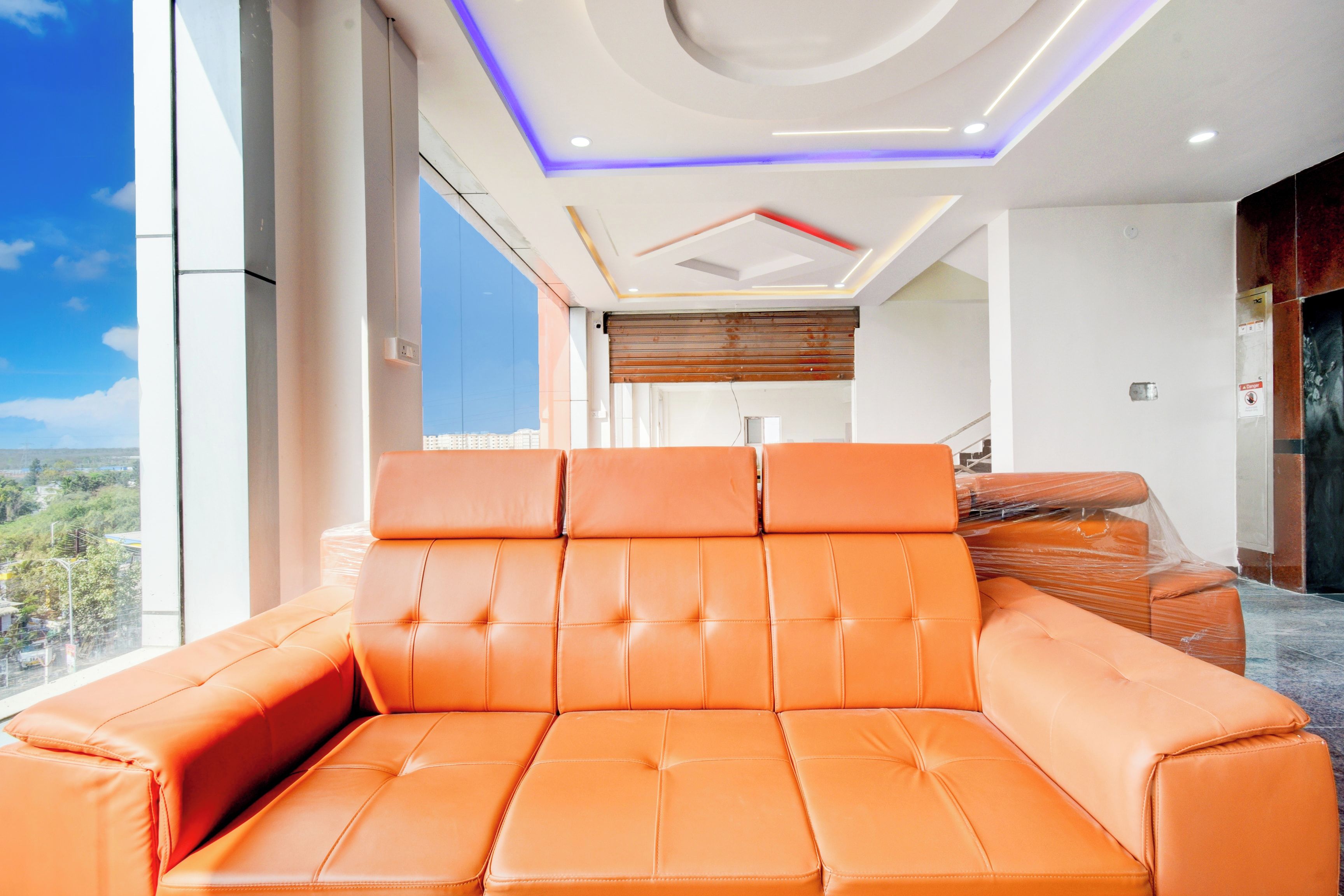 Un interior moderno con un sofá grande color naranja, vistas de la ciudad e iluminación empotrada en el techo.