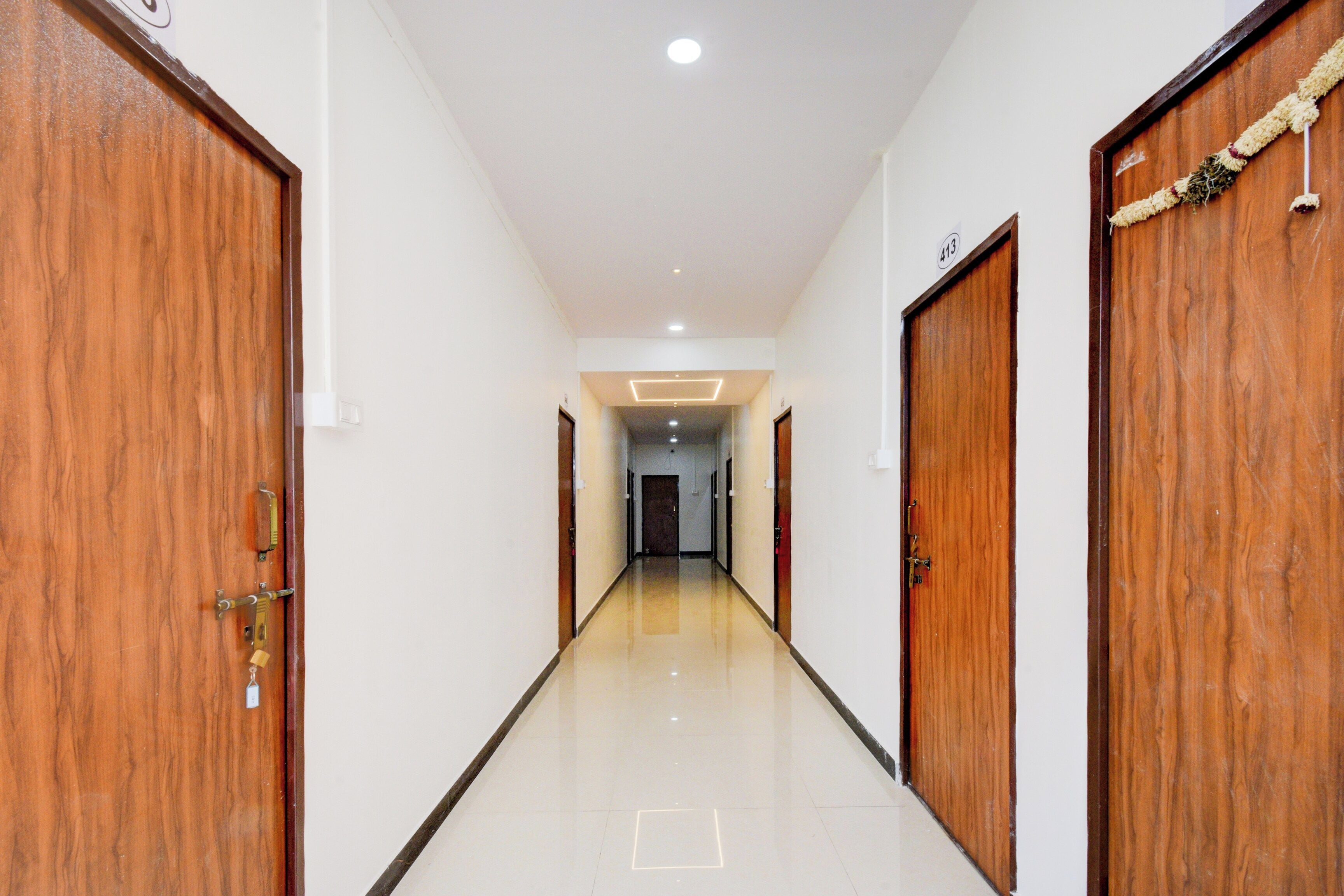 A corridor with wooden doors on both sides, a tiled floor, and a ceiling with recessed lighting.