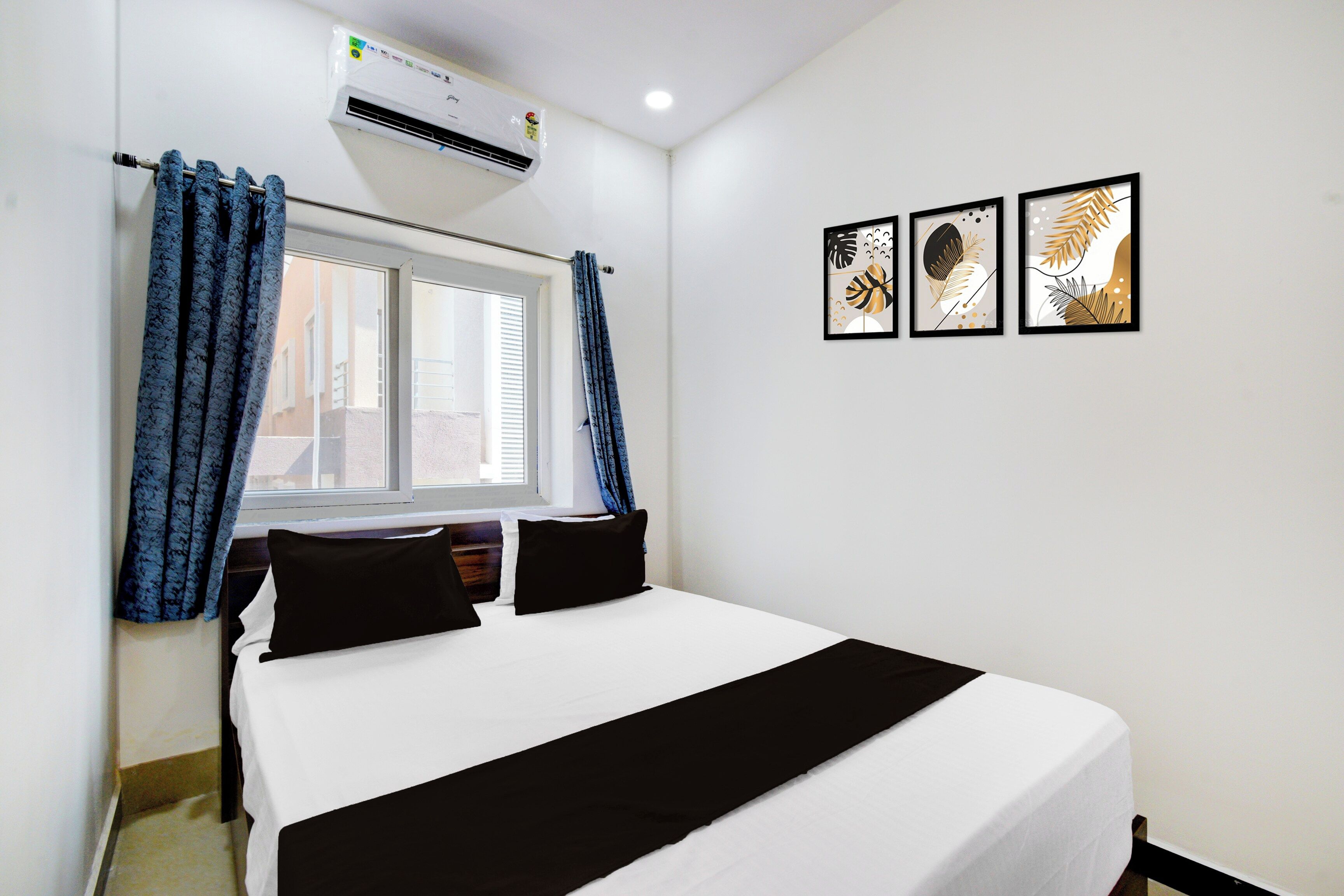 Quarto de hotel com uma cama, janela com cortinas, ar condicionado e três quadros na parede.