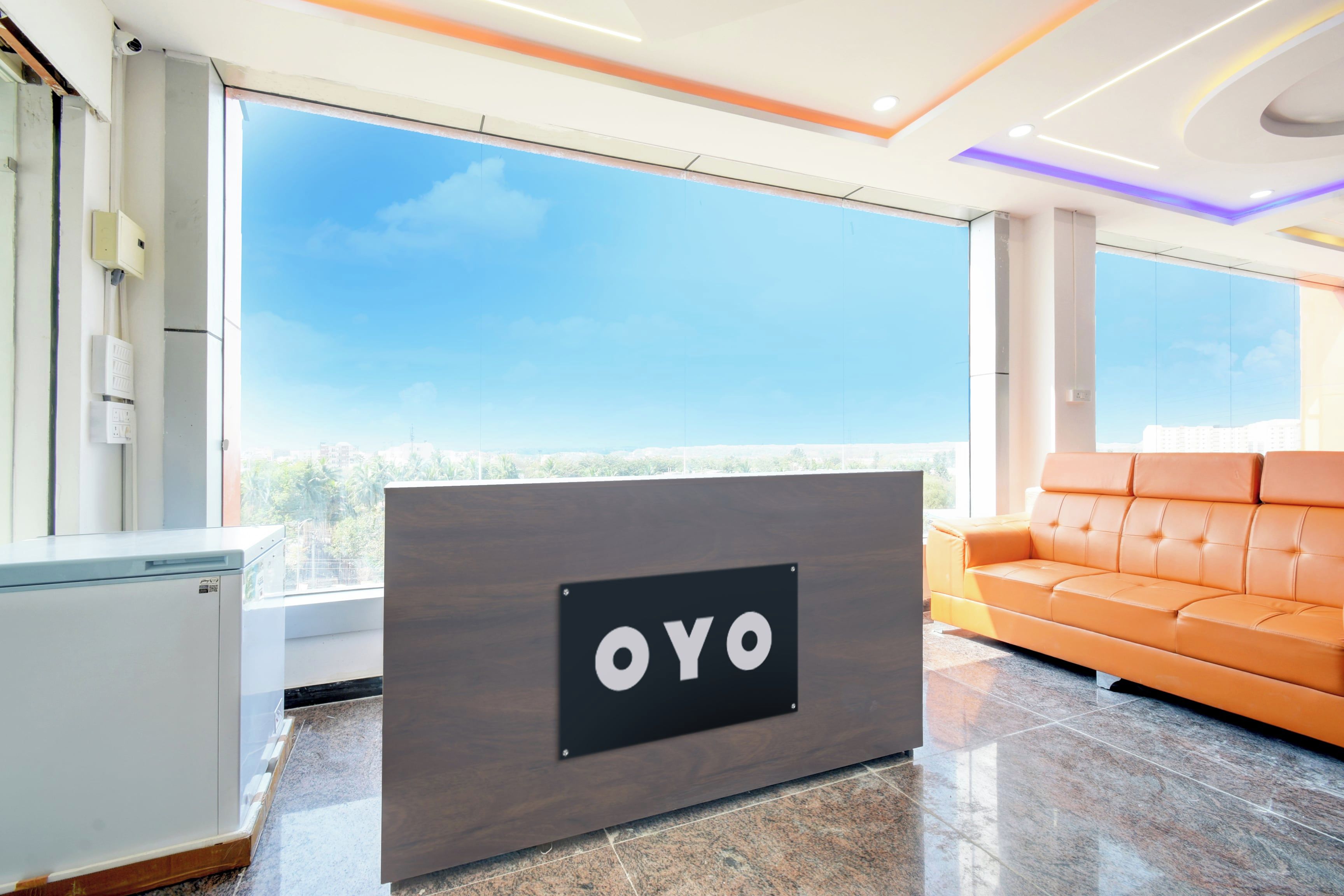 Una recepción con la marca 'OYO', un sofá moderno anaranjado y un amplio ventanal con vista a la ciudad.