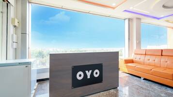Una recepción con la marca 'OYO', un sofá moderno anaranjado y un amplio ventanal con vista a la ciudad.