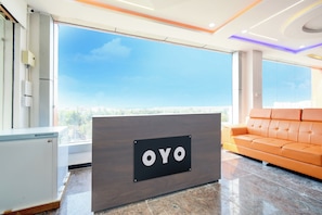 Una recepción con la marca 'OYO', un sofá moderno anaranjado y un amplio ventanal con vista a la ciudad.