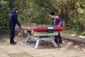 Two people playing foosball outdoors with a table and stands. - Type B "Zee, Bos en Duin" (Zoutelande)