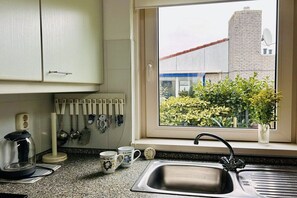 Una cucina con finestra, una moka, tazze e un lavandino.