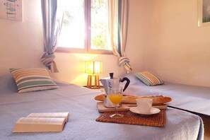 Una cama bien hecha con un libro, un vaso de zumo de naranja y una bandeja de desayuno con pan y una taza.