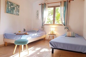 A room with two single beds, a small stool, a table with a lamp, and a window with curtains. - Holiday home with 2 bedrooms (Porto Vecchio)
