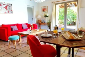 Ein helles Wohnzimmer mit einem roten Sofa, einem Holzespeise-Tisch mit Brot und Blick auf Grünfläche draußen.