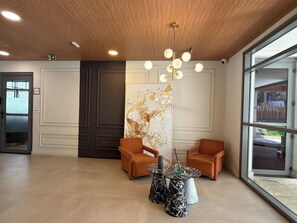 A modern lobby with two orange armchairs, a marble coffee table, and a large abstract painting on the wall. - 1BR w/ Queen Bed, Pool & Parking – Jardins near Metro PKS124 (São Paulo)