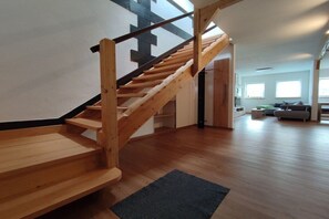 A wooden staircase leading to an upper level, a living area with a sofa and a coffee table, and a large window providing natural light. - Holiday apartment with 1 bedroom (Serrig)