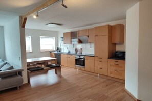 A modern kitchen with wooden cabinets, a dining table, and a built-in oven. - Holiday apartment with 1 bedroom (Serrig)