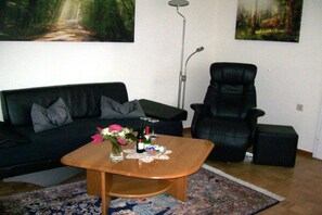A living room with a black leather sofa, a wooden coffee table with a vase of flowers, a black leather armchair, and a painting of a forest on the wall. - in a lovely location (72270 Baiersbronn, Deutschland)