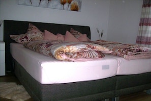 A bed with a floral bedspread and multiple pillows, a bedside table, and a wall-mounted artwork. - in a lovely location (72270 Baiersbronn, Deutschland)