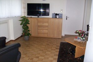 A living room with a television, wooden cabinet, potted plant, and a dining area with a table and chairs. - in a lovely location (72270 Baiersbronn, Deutschland)