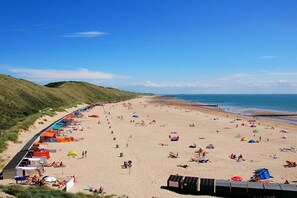 A beach with tents and beachgoers, a clear sky, and a hilly landscape in the background. - Holiday apartment with 1 bedroom (Zoutelande)