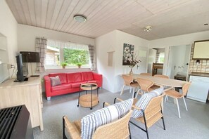 A cozy living area with a red sofa, wicker chairs, a dining table, and a kitchen area with a dishwasher. - Holiday apartment with 1 bedroom (Zoutelande)