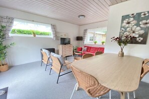 A room with a wooden dining table, wicker chairs, a red sofa, a television, and a painting on the wall. - Holiday apartment with 1 bedroom (Zoutelande)
