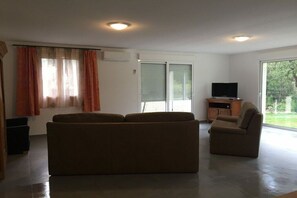 A living room with a sofa, a chair, a television, and a sliding glass door. - Holiday home in Les Salelles with bathtub (Les Salelles)