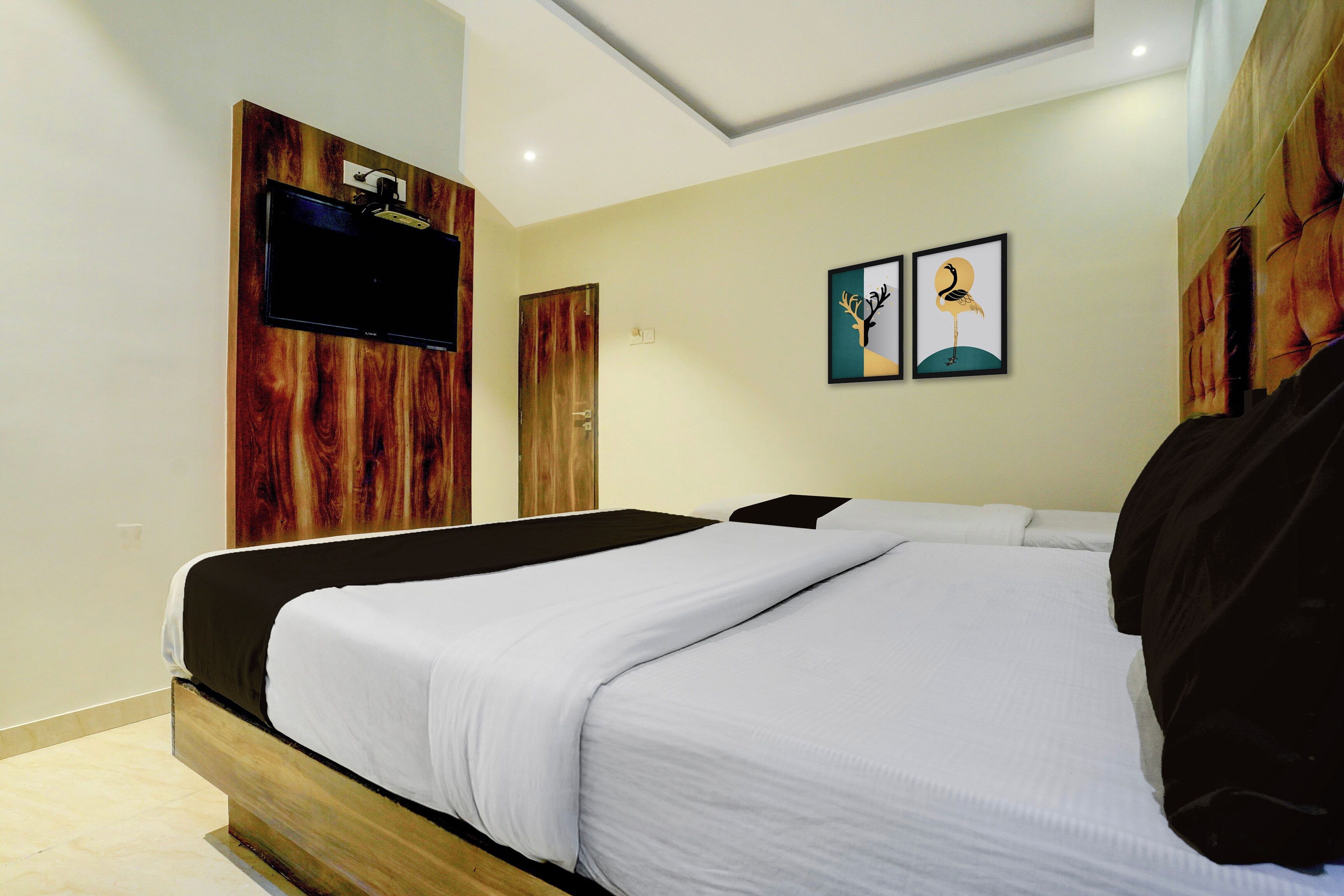 Una habitación de hotel con una cama, un televisor montado en un panel de madera y dos obras de arte enmarcadas en la pared.