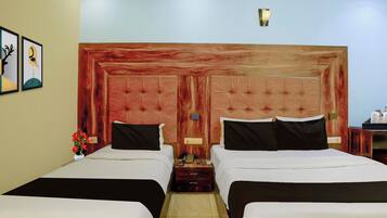 A hotel room with two beds, a wooden headboard, a nightstand, a vase with flowers, and a wall-mounted lamp.