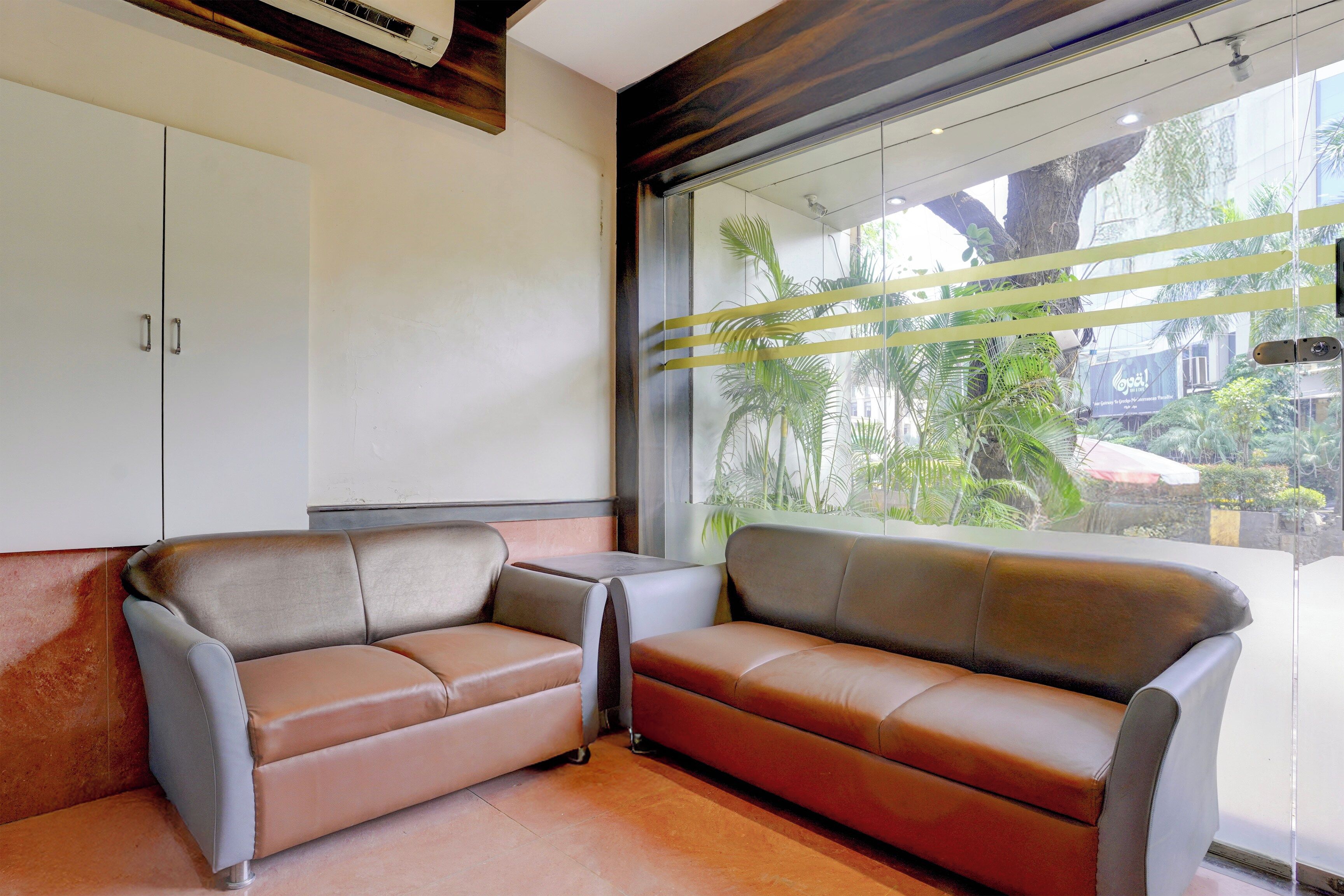A modern waiting area with two sofas, a cabinet, and a large window with a view of greenery.